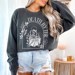May include: A black cropped sweatshirt with a white graphic of a skeleton reading a book with the text "Death by TBR" above the skeleton.