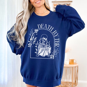 May include: Navy blue sweatshirt with a white graphic of a skeleton reading a book with the text "Death by TBR" above the skeleton.
