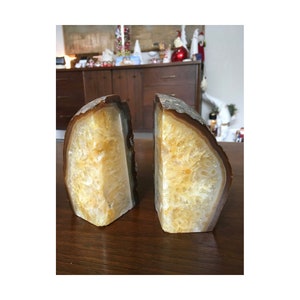 May include: A pair of agate bookends, each with a natural brown exterior and a yellow-toned interior. The bookends are shaped like half-spheres and have a rough, textured surface.