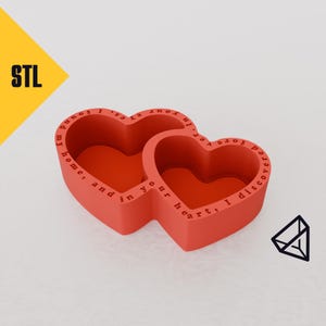 Puede incluir: Dos contenedores rojos en forma de corazón con un mensaje grabado en el exterior. El mensaje dice "He encontrado mi hogar, y en tu corazón, descubro la eternidad".