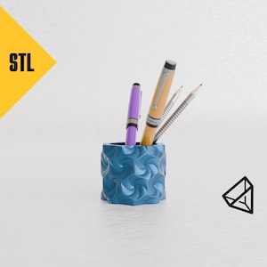 May include: A blue, textured, hexagonal pencil holder with three pens inside. The pens are purple, orange, and silver.
