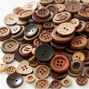Puede incluir: Una colección de botones de madera de varios tamaños y formas, en tonos marrones que van desde el beige claro hasta el marrón oscuro. Los botones tienen diseños de dos y cuatro agujeros. Algunos botones tienen detalles decorativos.