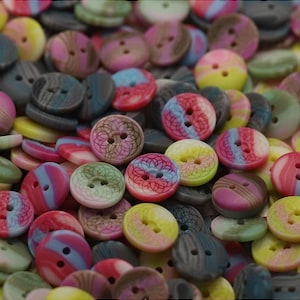 May include: A collection of colorful buttons in various shades of pink, blue, yellow, and green. The buttons have two holes and decorative patterns. The buttons are made of plastic and are suitable for sewing and craft projects.