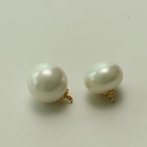 May include: Two white pearl earrings with gold-colored clasps. The pearls have a lustrous, iridescent sheen, reflecting light. The earrings are set against a plain, off-white background.