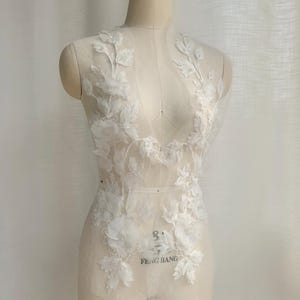 May include: White floral lace applique with 3D flower and leaf details. The applique is on a sheer mesh backing and is displayed on a mannequin. The text "FENG BANG" is visible at the bottom.
