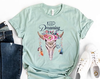 May include: A light blue t-shirt with a floral skull design and the text "Keep Dreaming".