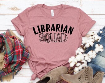 May include: A mauve colored t-shirt with the text "LIBRARIAN SQUAD" in black lettering.