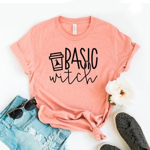 May include: A peach-colored t-shirt with a black graphic that says "Basic Witch" with a coffee cup with a witch's hat on top.