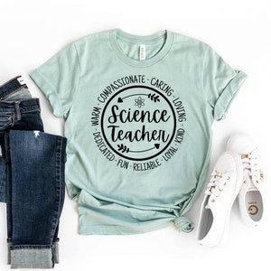 May include: A light blue t-shirt with a black circle design that says "Science Teacher" with a black atom symbol and leaves. The circle is surrounded by the words "Warm - Compassionate - Caring - Loving - Dedicated - Fun - Reliable - Loyal - Kind".