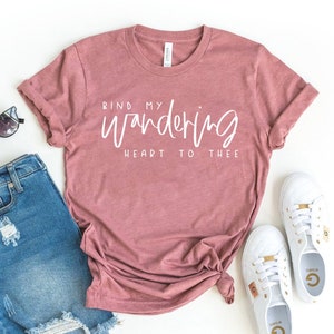 Könnte beinhalten: Ein staubiges rosafarbenes T-Shirt mit dem Text "Bind my wandering heart to thee" in weißen Buchstaben.