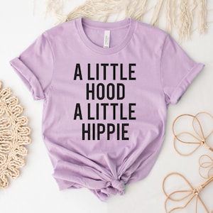 May include: A lavender t-shirt with black text that reads "A little hood a little hippie".