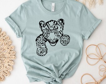 Può includere: Una maglietta blu chiaro con una grafica nera di un cucciolo di leopardo che spunta da dietro il tessuto.