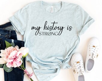 Könnte beinhalten: Ein hellblaues T-Shirt mit dem Text "my history is strong" in schwarzer Schrift.
