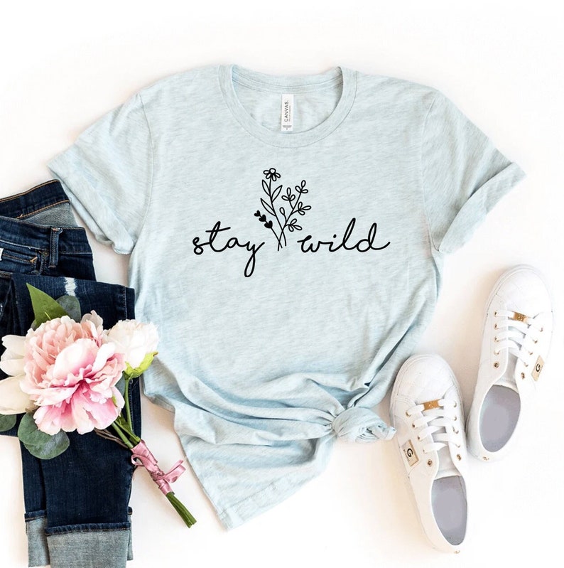 May include: A light blue t-shirt with a floral design and the text "stay wild" in black.