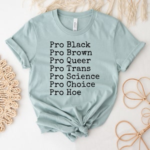 Puede incluir: Una camiseta azul claro con el texto "Pro Black, Pro Brown, Pro Queer, Pro Trans, Pro Science, Pro Choice, Pro Hoe" impreso en negro.