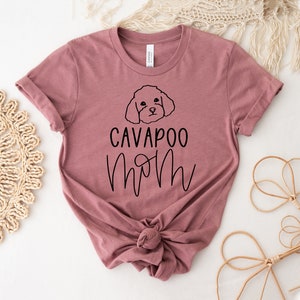 May include: A mauve t-shirt with a black outline of a cavapoo dog and the text "Cavapoo Mom" in black.
