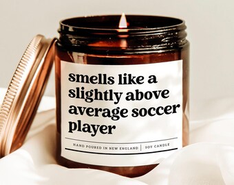 May include: A lit soy candle in a brown glass jar with a copper lid. The label reads "smells like a slightly above average soccer player." The candle is hand-poured in New England.