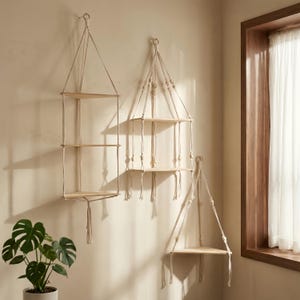 May include: Three hanging wooden shelves with natural rope supports. The shelves are different sizes and have a minimalist design. The shelves are suspended from the ceiling and are ideal for displaying plants or decorative items.
