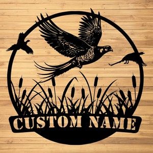 May include: Black metal silhouette of a pheasant flying over a bed of reeds with the text "CUSTOM NAME" at the bottom.