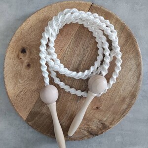 Peut inclure: Une corde à sauter en coton blanc avec des poignées en bois. La corde est enroulée sur une surface en bois.