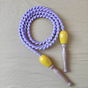 Peut inclure: Une corde à sauter violette avec des poignées en bois jaune. La corde est torsadée et les poignées sont arrondies.