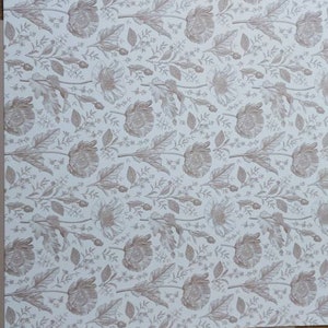 May include: A sheet of white paper with a repeating pattern of brown floral designs. The paper is on top of a piece of brown cardboard.