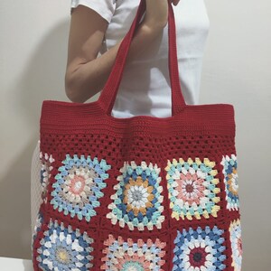 May include: Red crochet tote bag with colorful granny square patches. The bag has two long straps and a spacious interior.