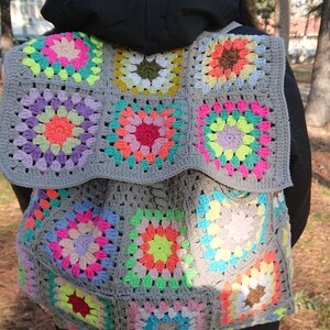 Op de afbeelding: Een grijze gehaakte tas met kleurrijke granny squares. De tas is gemaakt met een verscheidenheid aan felle kleuren, waaronder roze, groen, geel en blauw.