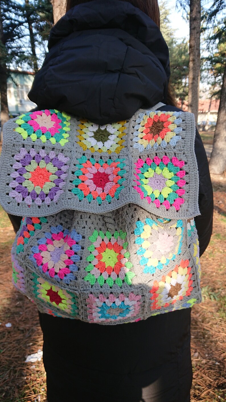 Op de afbeelding: Een grijze gehaakte tas met kleurrijke granny squares. De tas is gemaakt met een verscheidenheid aan felle kleuren, waaronder roze, groen, geel en blauw.