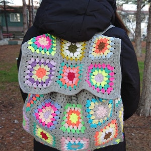 May include: A gray crochet backpack with colorful granny squares. The backpack is made with a variety of bright colors, including pink, yellow, green, blue, and orange.