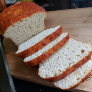 May include: A loaf of sliced white bread on a wooden chopping board. The bread is light brown and has a slightly crispy crust. The slices are stacked on top of each other.