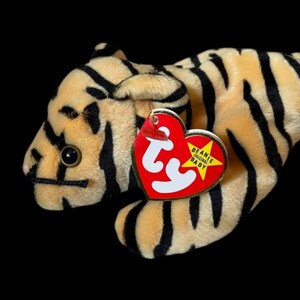 May include: A plush tiger toy with a tan body and black stripes. The toy has a red heart-shaped tag with white text and a yellow star. The tiger's eyes are black, and it has a black stitched nose.