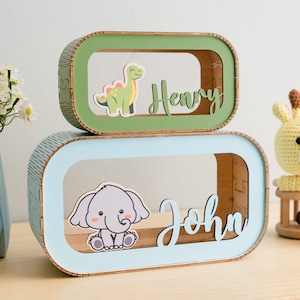 May include: Two wooden boxes stacked on top of each other. The top box is green and has a dinosaur cutout with the name "Henry" written on it. The bottom box is blue and has an elephant cutout with the name "John" written on it.