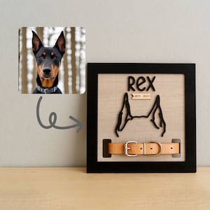 May include: A wooden memorial plaque with a black frame, featuring the name "Rex" and the years "2015-2021". The design includes a cutout of dog ears and a tan leather collar with a silver buckle. An image of a dog is in the upper left corner.