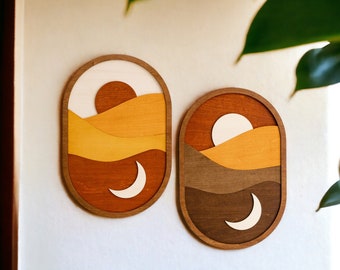 Könnte beinhalten: Zwei Wanddekorationen aus Holz mit einem mehrschichtigen Design in Braun, Orange und Gelb. Jedes Stück zeigt einen weißen Halbmond und einen weißen Kreis.