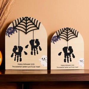 Pode incluir: Duas decorações de Halloween em madeira. Cada uma apresenta uma teia de aranha preta, uma aranha roxa e aranhas de pegadas pretas. O texto diz "Happy Halloween 2025" e "The sweetest spiders you'll ever meet!" Gráficos de fantasmas brancos também estão incluídos.