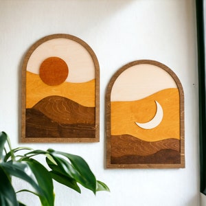 Pu&ograve; includere: Due opere d'arte da parete in legno. Una raffigura un sole, l'altra una luna crescente. Entrambe presentano un design paesaggistico a strati nei toni del marrone, arancione e crema, incorniciate in cornici ad arco. Il sole &egrave; un cerchio arancione pieno.
