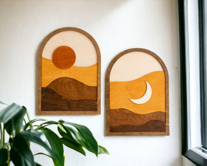 Pu&ograve; includere: Due opere d'arte da parete in legno. Una raffigura un sole, l'altra una luna crescente. Entrambe presentano un design paesaggistico a strati nei toni del marrone, arancione e crema, incorniciate in cornici ad arco. Il sole &egrave; un cerchio arancione pieno.