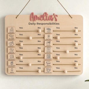 Può includere: Una tabella di responsabilità quotidiane in legno con il nome "Amelia's" in corsivo rosa. La tabella include icone per attività come "Fai la doccia" e "Lettura", con cursori per indicare "Sì" o "No".