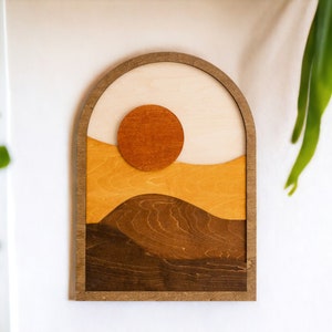Pu&ograve; includere: Arte da parete in legno con un design paesaggistico a strati. L'opera d'arte comprende un sole, colline e una cornice a forma di arco. La tavolozza dei colori &egrave; composta da toni caldi, tra cui marrone, arancione e beige. Questo pezzo &egrave; per l'arredamento murale.