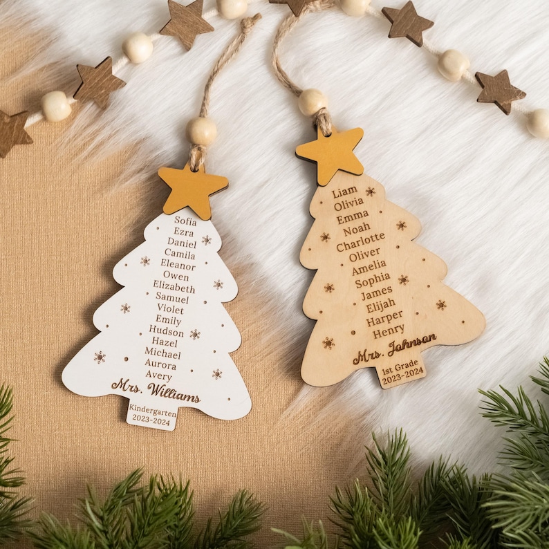 May include: Two wooden Christmas tree ornaments with student names and teacher names. The ornaments are decorated with a gold star and snowflakes. The text on the ornaments reads "Mrs. Williams Kindergarten 2023-2024" and "Mrs. Jahnsan 1st Grade 2023-2024".