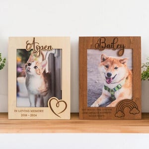 May include: Two wooden photo frames, one light and one dark, each with a pet photo. The light frame has a cat photo with the name "Aspen" and the text "In Loving Memory 2016-2024". The dark frame has a dog photo with the name "Bailey" and a rainbow.