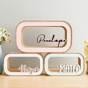May include: Three wooden boxes with cutout windows and personalized names. The top box is pink with the name "Penelope", the middle box is white with the name "Harper", and the bottom box is light green with the name "Mateo".