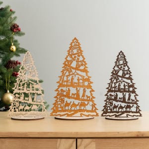 May include: Three wooden Christmas tree ornaments with intricate cutouts depicting the Nativity scene. The trees are in different sizes and are made of natural wood.