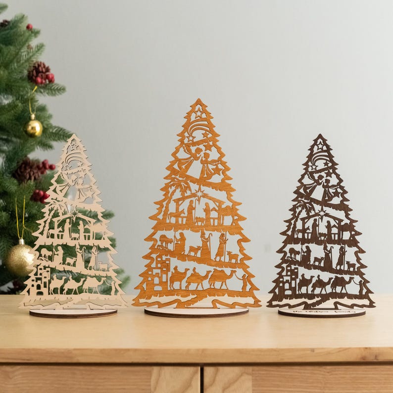 May include: Three wooden Christmas tree ornaments with intricate cutouts depicting the Nativity scene. The trees are in different sizes and are made of natural wood.