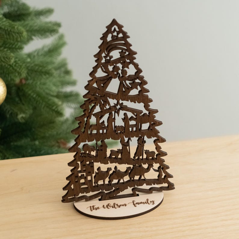 May include: A wooden Christmas tree ornament with a nativity scene cutout. The base of the tree is personalized with the text "The Wilson Family".
