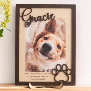 May include: A framed photo of a dog with the name "Gracie" in a wooden frame. The frame has a paw print cutout and the text "BEST FRIENDS COME INTO OUR LIVES AND LEAVE PAWPRINTS ON OUR HEARTS".