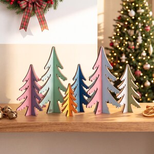 May include: A set of six freestanding wooden tree ornaments in various sizes and colours, including purple, light green, orange, dark blue, pink, and white. Each tree features a stylised, jagged silhouette with a flat base for stable display.
