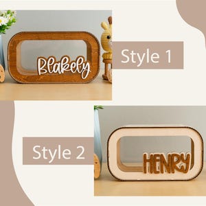 May include: Two wooden boxes with a cutout in the front. The boxes are made of natural wood and have a light brown finish. The first box has the name "Blakely" written in white letters on the front. The second box has the name "Henry" written in brown letters on the front. The boxes are labelled "Style 1" and "Style 2".