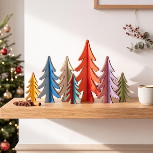 May include: A collection of eight freestanding wooden tree ornaments in various sizes and colours, including yellow, blue, beige, teal, orange, pink, and green. The trees feature a stylised, jagged silhouette and are arranged in a row.
